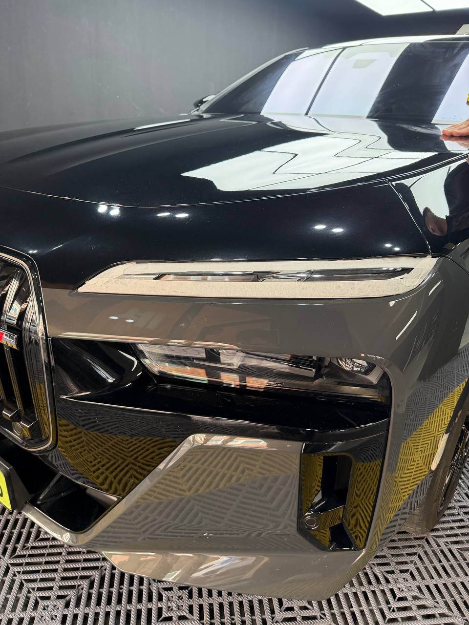 작업장 조명이 비친 유광 블랙 보닛과 헤드라이트. 블랭크랩에서 투톤으로 랩핑 중인 BMW i7 M70