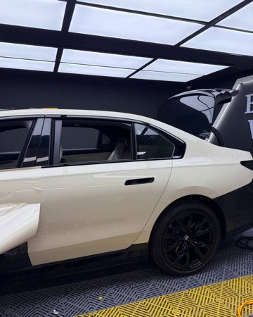 작업 중: 차체 옆면을 아이보리 필름으로 감싸는 중인 BMW i7 M70 옆모습. 열린 트렁크는 검은색
