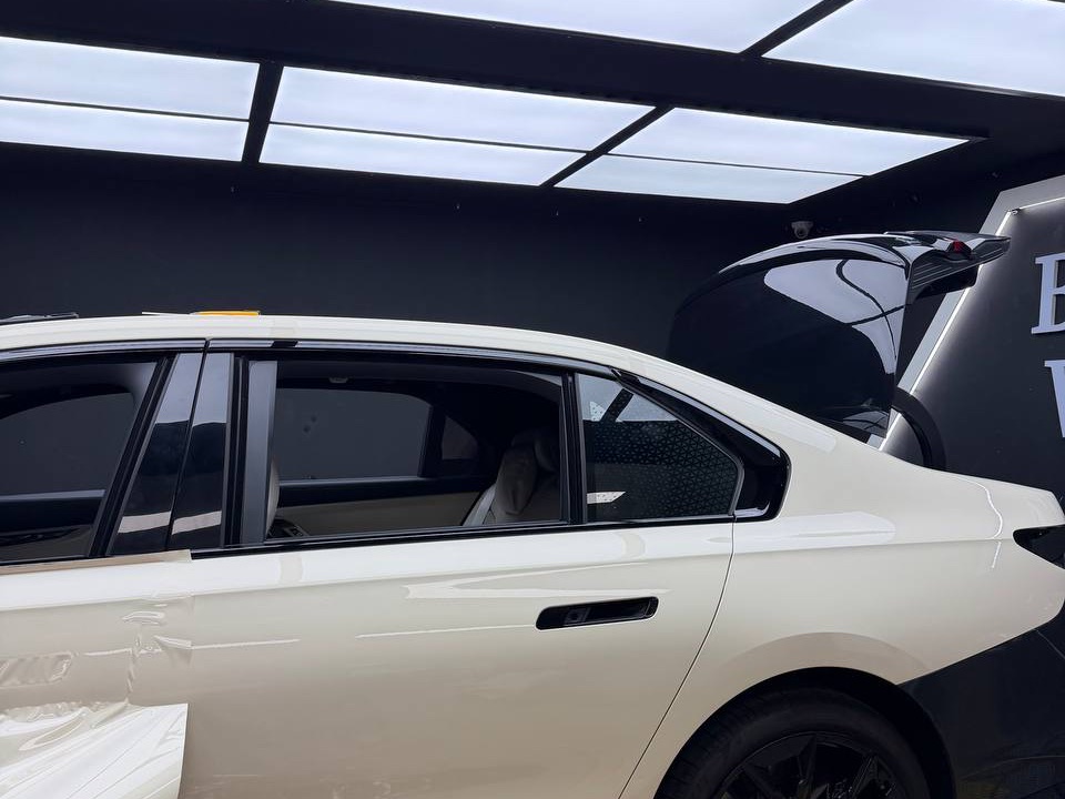천장 조명 아래 아이보리 · 블랙 투톤으로 랩핑 중인 BMW i7 M70이 서 있는 블랭크랩 작업장